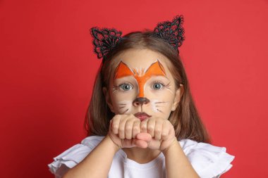 Yüzü boyalı ve kulakları kırmızı arka planda kedi gibi olan tatlı bir kız.