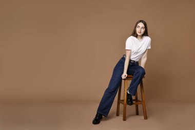 Kahverengi arka planda taburede oturan şık kotlu bir kadın. Metin için boşluk