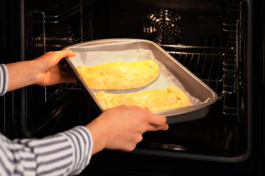 Yanmamış calzone pizzayla tabağı fırına koyan kadın, yakın plan.