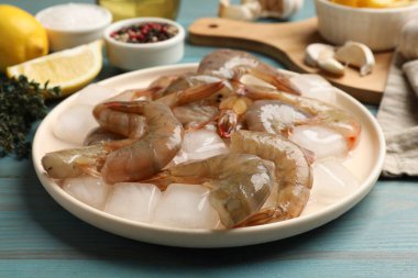 Taze çiğ karidesler, buz küpleri ve baharatlar açık mavi ahşap masada, yakın plan.