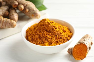 Aromatik zerdeçal tozu ve beyaz ahşap masa üzerinde taze kökler, yakın plan.