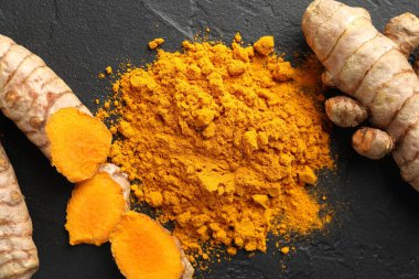 Aromatik zerdeçal tozu ve siyah masanın üzerinde taze kökler.