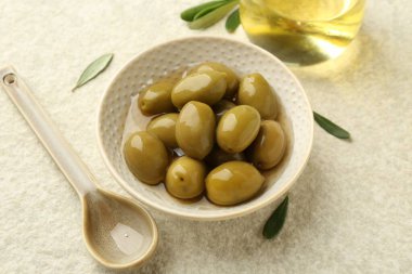 Lezzetli yeşil zeytinler kasede, yapraklar ve yağ bej masada, yakın plan.