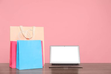 İnternet alışverişi. Laptop ve renkli kağıt torbaları pembe arka plana karşı ahşap masada.