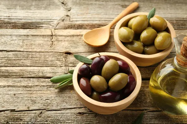 Lezzetli salamura edilmiş zeytinler, yeşil yapraklar, ahşap masada kaşık ve yağ, yakın çekim. Metin için boşluk