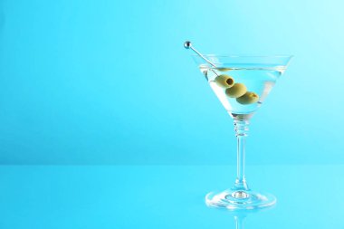 Açık mavi arka planda zeytinli martini kokteyli, metin için boşluk