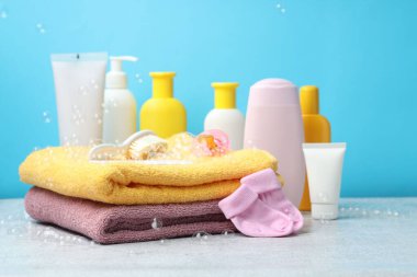 Bebek kozmetik ürünleri, çoraplar, banyo aksesuarları ve açık mavi arka planda gri desenli masada uçan baloncuklar.