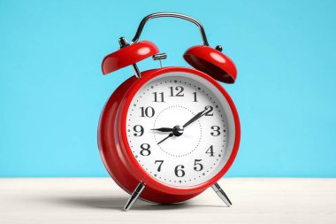 Beyaz ahşap masada açık mavi zemin üzerinde bir kırmızı alarm saati