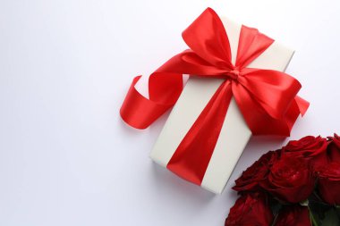 Kırmızı fiyonklu hediye kutusu ve beyaz arka planda güzel güller, düz yatıyordu. Metin için boşluk
