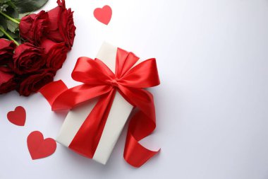 Kırmızı fiyonklu hediye kutusu, beyaz arka planda güzel güller ve kağıt kalpler, düz yatış. Metin için boşluk