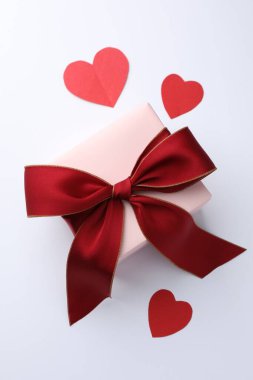 Kırmızı fiyonklu hediye kutusu ve beyaz zemin üzerinde kağıt kalpler, düz yatıyordu.
