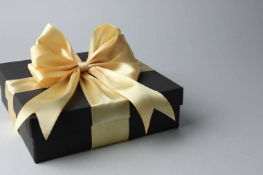 Gri arka planda altın fiyonklu hediye kutusu, yakın plan. Metin için boşluk