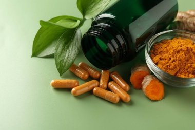 Kasedeki zerdeçal tozu, kapsüller ve ters çevrilmiş tıbbi şişe, yakın plan.