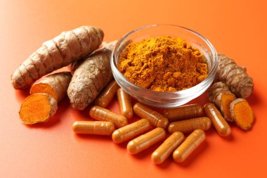 Kavanozda zerdeçal tozu, turuncu arka planda kök ve kapsüller, yakın plan.