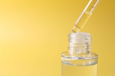 Sarı arka planda pipetten şişeye serum damlatıyorlar. Yakın plan. Metin için boşluk