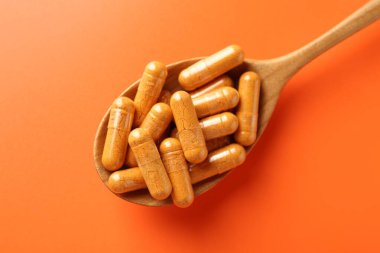 Turuncu arka planda ahşap kaşık içindeki zerdeçal kapsülleri.