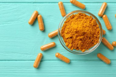 Turkuaz ahşap masa üzerinde zerdeçal kapsülleri ve pudra düz yerde. Metin için boşluk