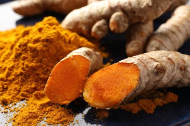 Aromatik zerdeçal tozu ve mavi tabakta taze kökler, yakın plan.