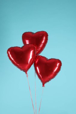 Açık mavi arka planda üç kırmızı kalp şeklinde balon. Sevgililer Günün kutlu olsun.