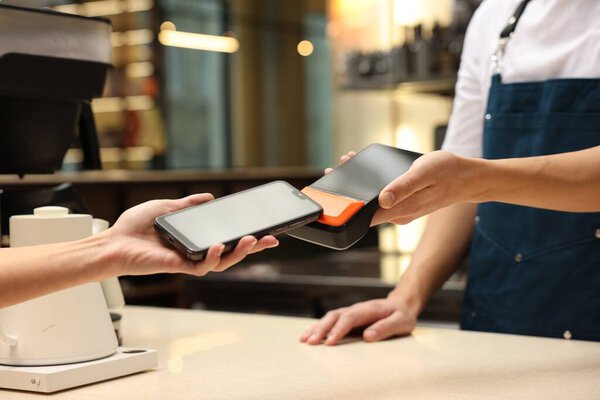 Woman paying with smartphone via terminal in cafe, closeup