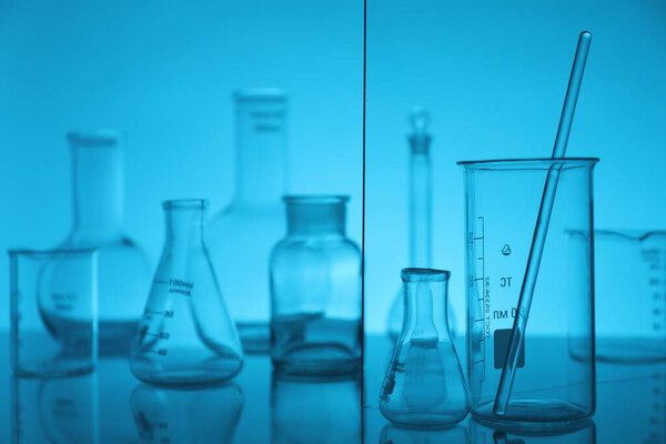 Laboratory glassware on mirror surface against light blue background