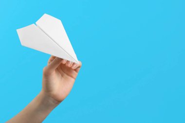 Açık mavi arka planda beyaz kağıt uçaklı kadın, yakın plan. Metin için boşluk