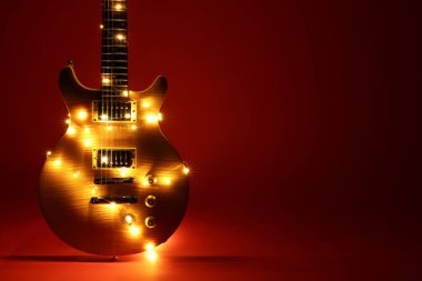 Koyu kırmızı arka planda Noel ışıkları olan elektro gitar.