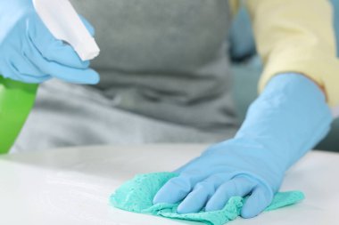 Kadın temizlik malzemesi kullanıyor. Masayı içerideki paçavralarla siliyor. Yakın plan.