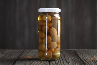 Cam kavanozda yeşil zeytin turşusu. Ahşap masada, gri arka planda.