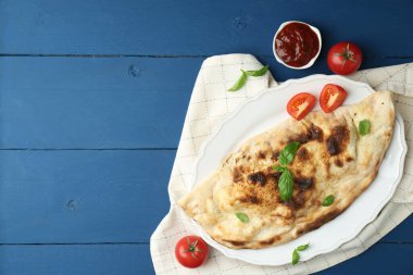 Fesleğenli, domatesli ve mavi ahşap masadaki soslu leziz bir calzone. Metin için boşluk
