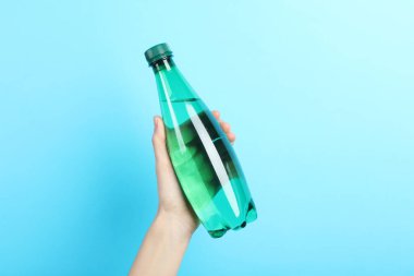 Açık mavi arka planda plastik su şişesi tutan kadın, yakın plan.