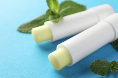 Açık mavi arka planda doğal dudak kremleri ve nane yaprakları, yakın plan.