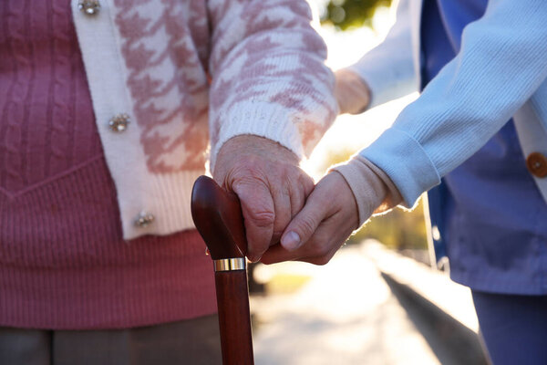 Elderly woman with walking cane and her caregiver in park, closeup
