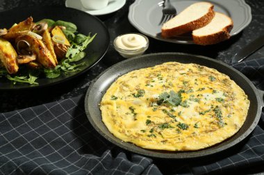 Lezzetli bir kahvaltı. Lezzetli omlet ve kızarmış patates siyah desenli masada servis edilir.