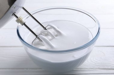 Krem şanti ile karıştırıcı beyaz ahşap masada, yakın plan.