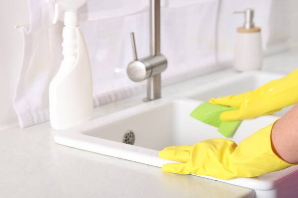 Woman cleaning sink with rag in kitchen, closeup