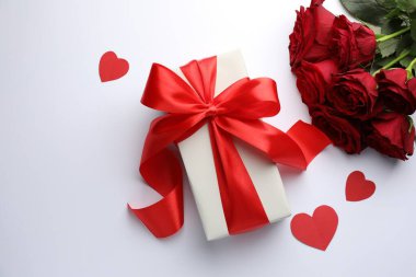 Kırmızı fiyonklu hediye kutusu, beyaz arka planda güzel güller ve kağıt kalpler, düz uzanmış