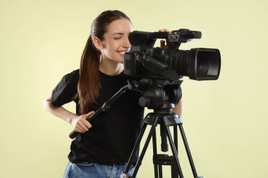 Soluk zeytinli arka planda profesyonel video kamerası olan mutlu kadın.