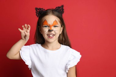 Yüzü ve kulakları kırmızı arka planda kedi gibi boyalı tatlı bir kız, mesaj için yer var.