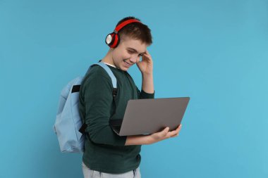 Sırt çantası, kulaklığı ve dizüstü bilgisayarı açık mavi arka planda olan genç çocuk.