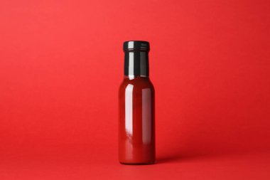 Kırmızı arka planda cam şişede ketçap.