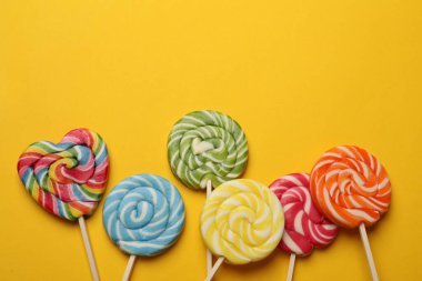 Sarı arka planda leziz lolipoplar, düz yatış. Metin için boşluk