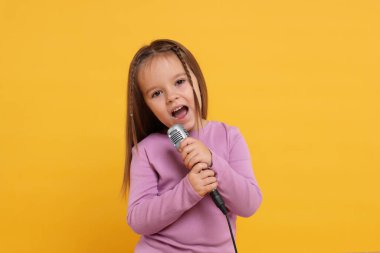 Turuncu arka planda mikrofonlu şirin kız şarkı söylüyor.