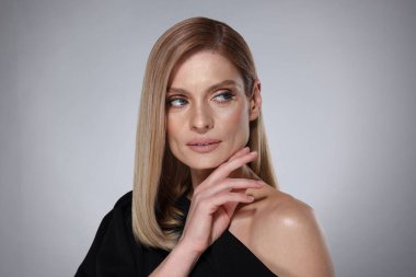 Gri arka planda düz sarı saçlı güzel bir kadının portresi.