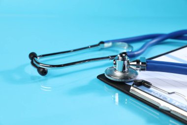 Açık mavi arkaplanda stetoskop ve sağlık kartı formu, yakın plan.
