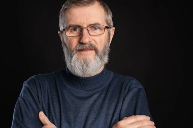 Siyah arka planda çapraz kollu olgun bir adamın portresi.