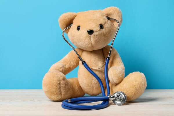 Pediatrics concept. Teddy bear with stethoscope on wooden table against light blue background