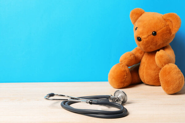 Pediatrics concept. Teddy bear with stethoscope on wooden table against light blue background, space for text