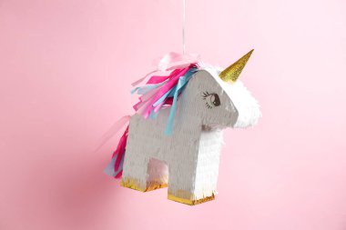 Pembe arka planda asılı tek boynuzlu at şeklinde parlak bir pinata.
