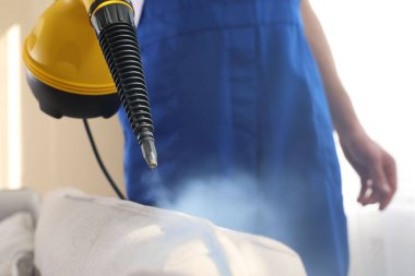 Temizlikçi kanepeyi evde buharlı temizleme makinesiyle temizliyor.